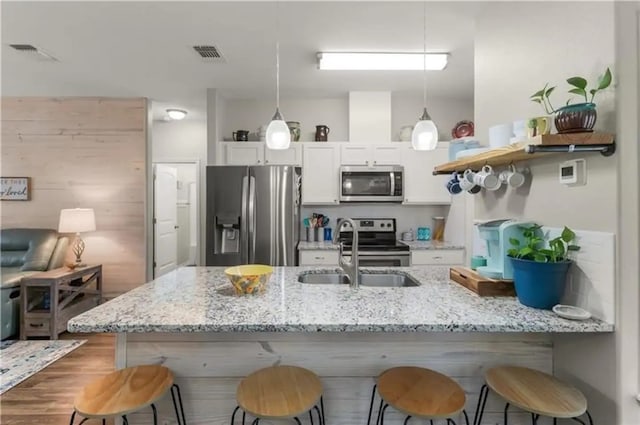 kitchen with white cabinetry, stainless steel appliances, a kitchen breakfast bar, hanging light fixtures, and light stone countertops