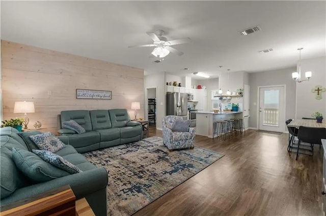 living room with dark hardwood / wood-style flooring, ceiling fan with notable chandelier, wood walls, and sink