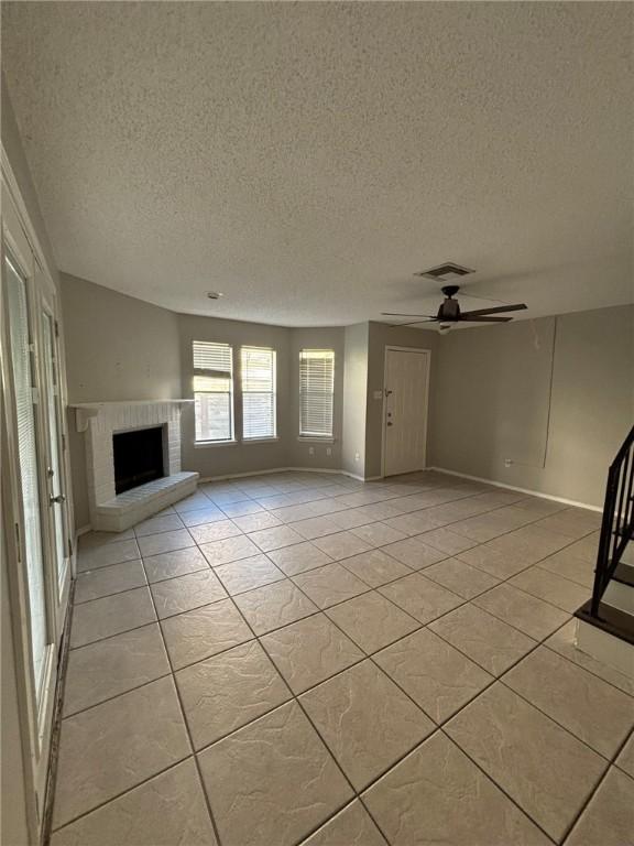 4401 River Valley Dr Unit 503, Corpus Christi, TX 78410 - unfurnished living room featuring light tile patterned floors, a brick fireplace, ceiling fan, and a textured ceiling
