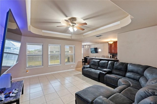 living room featuring light tile patterned floors, ceiling fan with notable chandelier, a tray ceiling, and ornamental molding