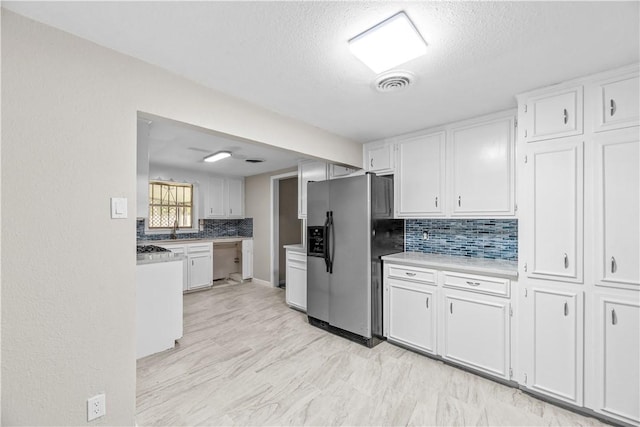 5611 Nelson, Corpus Christi, TX 78411 - kitchen featuring stainless steel refrigerator with ice dispenser, tasteful backsplash, white cabinetry, a textured ceiling, and light countertops