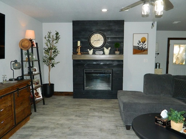 living room featuring ceiling fan, a fireplace, and light wood-type flooring