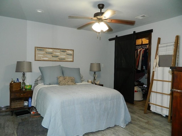 bedroom with a closet, hardwood / wood-style flooring, a barn door, and ceiling fan