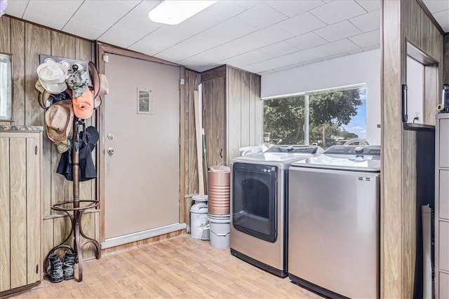 clothes washing area featuring washing machine and clothes dryer, wooden walls, and light hardwood / wood-style flooring