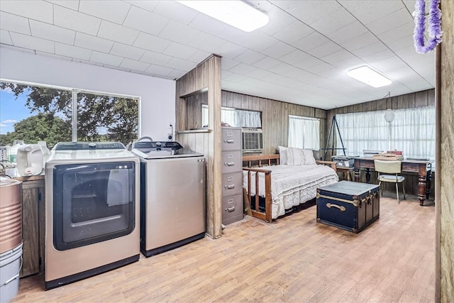 clothes washing area with light wood-type flooring, wooden walls, and washing machine and clothes dryer