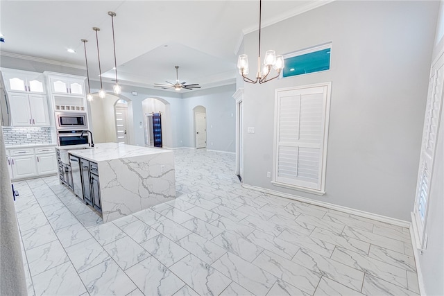 kitchen featuring appliances with stainless steel finishes, ceiling fan with notable chandelier, pendant lighting, a center island with sink, and white cabinetry