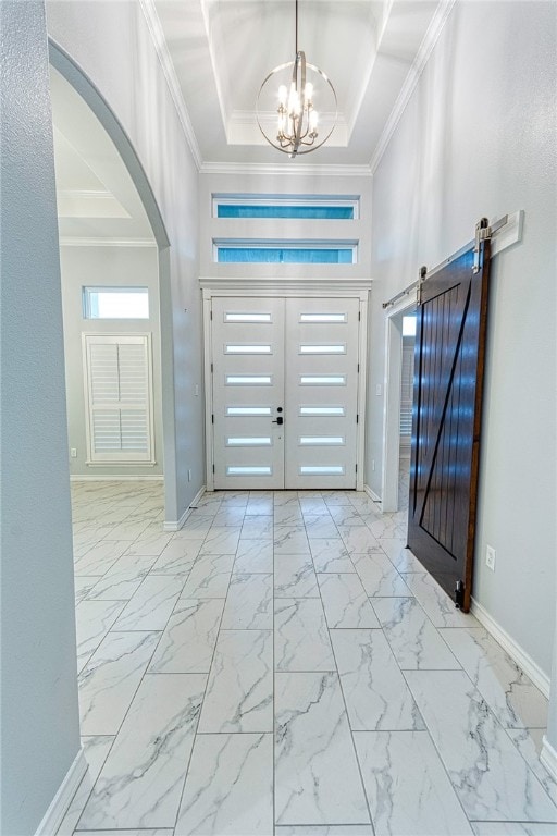 entryway featuring a raised ceiling, a barn door, crown molding, and a notable chandelier