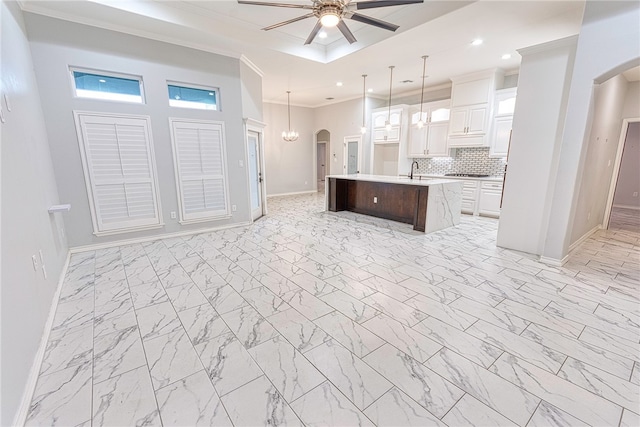 kitchen featuring decorative backsplash, ceiling fan, pendant lighting, white cabinetry, and an island with sink