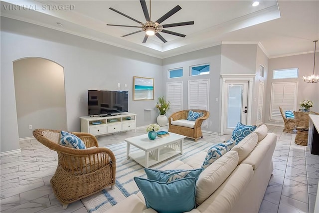 living room with a towering ceiling, ceiling fan with notable chandelier, a tray ceiling, and ornamental molding