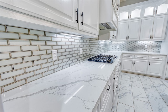 kitchen featuring decorative backsplash, light stone countertops, custom range hood, white cabinetry, and stainless steel gas cooktop