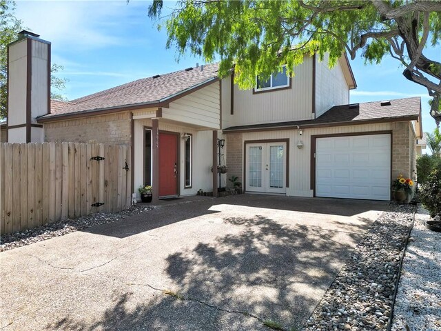 view of front of house featuring an attached garage, fence, concrete driveway, brick siding, and french doors