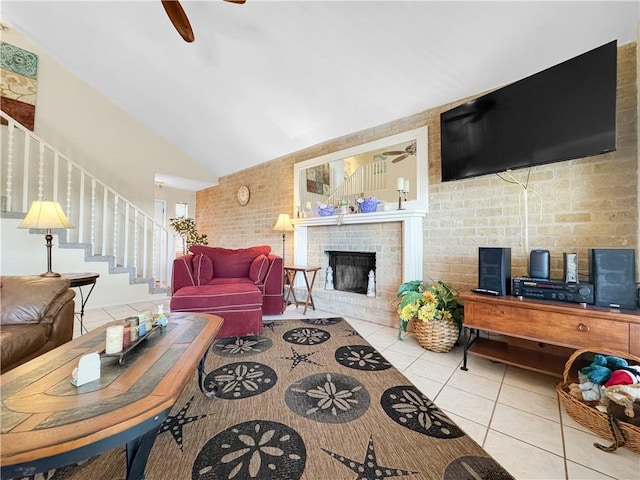 living area with tile patterned floors, a fireplace, a ceiling fan, stairs, and high vaulted ceiling