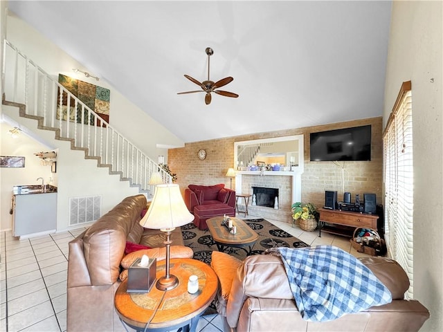 tiled living room featuring high vaulted ceiling, ceiling fan, visible vents, stairway, and a brick fireplace