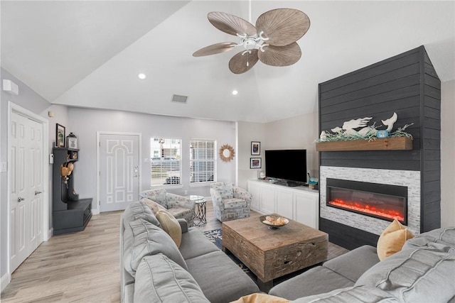 living area with lofted ceiling, recessed lighting, a ceiling fan, light wood finished floors, and a glass covered fireplace