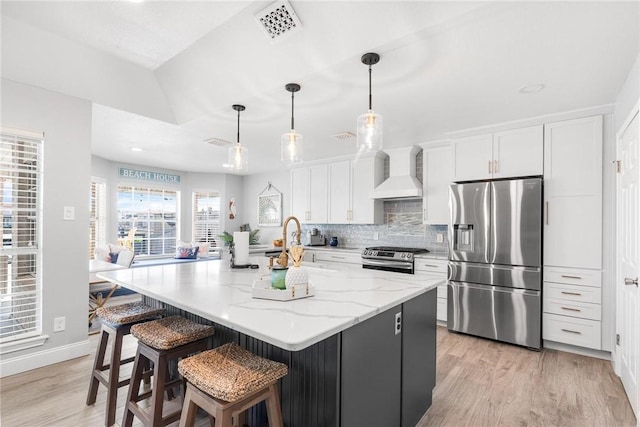 kitchen with stainless steel appliances, wall chimney exhaust hood, visible vents, and white cabinets