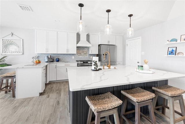 kitchen featuring premium range hood, visible vents, a kitchen breakfast bar, appliances with stainless steel finishes, and decorative backsplash