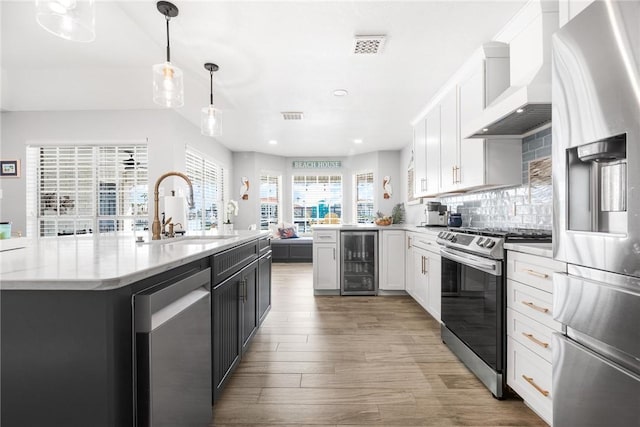 kitchen featuring custom exhaust hood, tasteful backsplash, appliances with stainless steel finishes, a sink, and beverage cooler