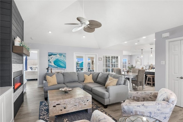 living room featuring a large fireplace, vaulted ceiling, french doors, light wood-type flooring, and recessed lighting