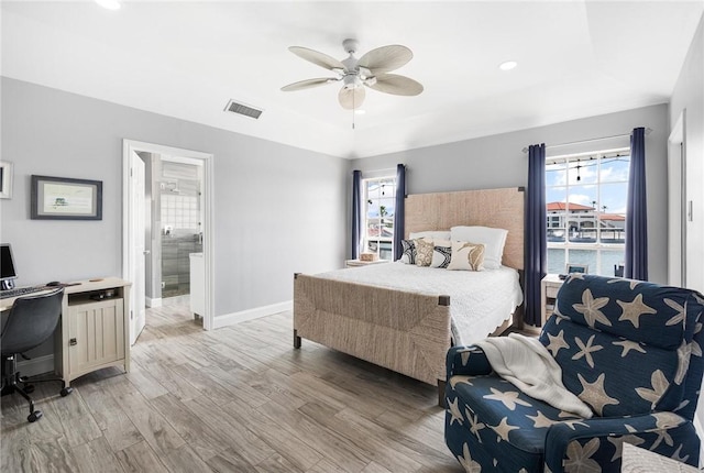 bedroom featuring ensuite bathroom, visible vents, baseboards, light wood finished floors, and a raised ceiling