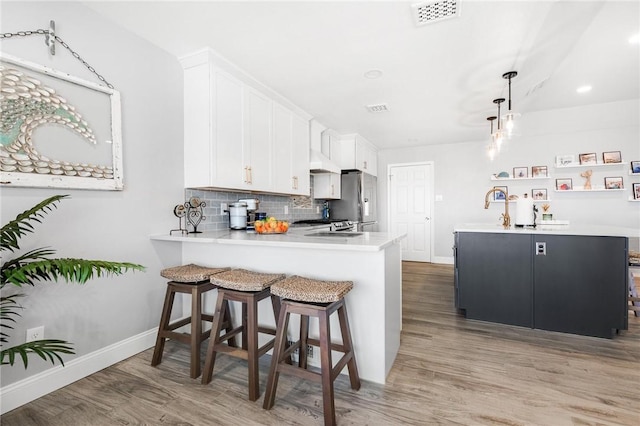 kitchen with light wood finished floors, tasteful backsplash, visible vents, light countertops, and under cabinet range hood