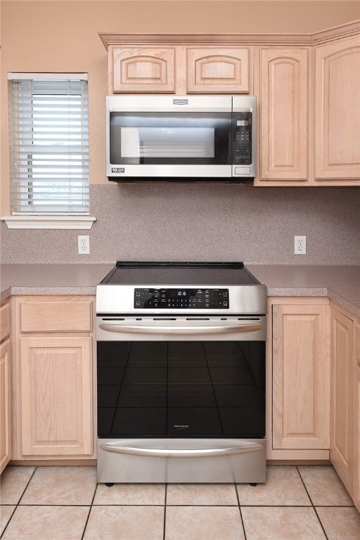 kitchen with stainless steel appliances, light brown cabinetry, light tile patterned floors, and decorative backsplash