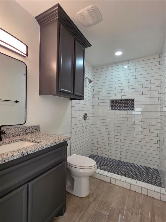 bathroom featuring a tile shower, visible vents, toilet, and vanity