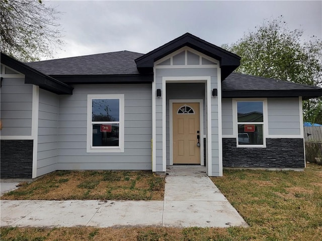 exterior space with stone siding and roof with shingles