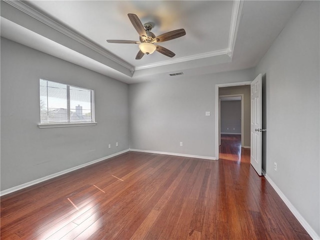 empty room with visible vents, baseboards, a tray ceiling, wood-type flooring, and crown molding