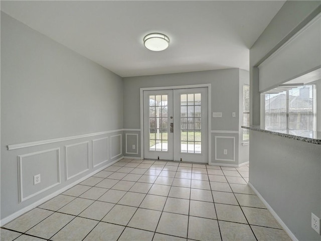 doorway featuring light tile patterned floors, a decorative wall, french doors, and a wainscoted wall