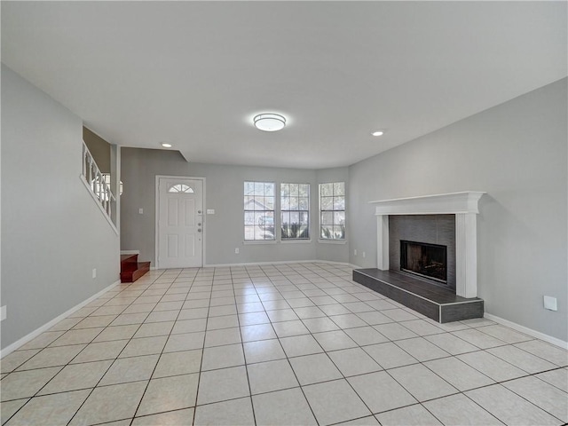 unfurnished living room featuring a tiled fireplace, light tile patterned flooring, baseboards, and stairs