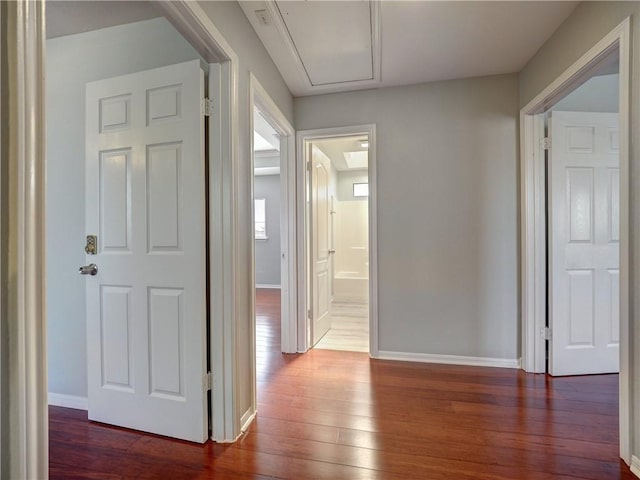 hall with attic access, baseboards, and wood-type flooring