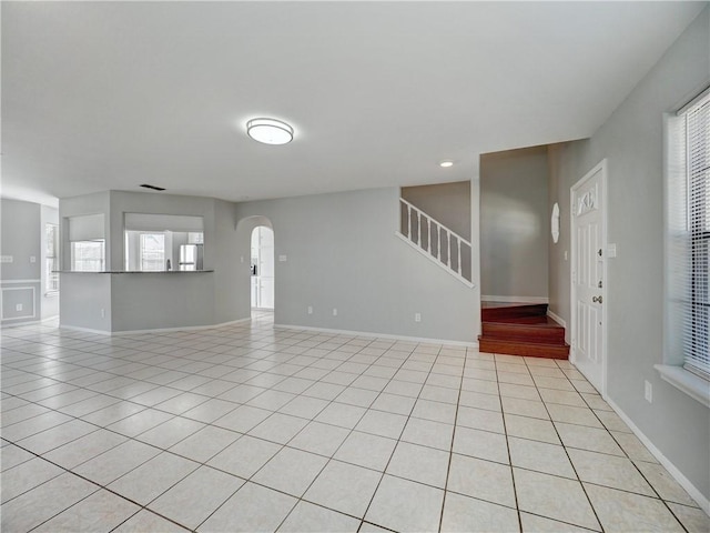 unfurnished living room featuring stairway, light tile patterned floors, baseboards, and arched walkways