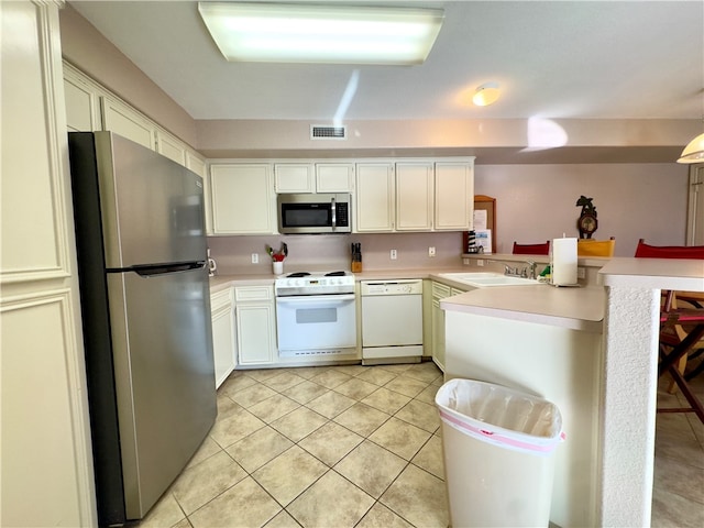 kitchen with sink, light tile patterned flooring, kitchen peninsula, white cabinets, and appliances with stainless steel finishes