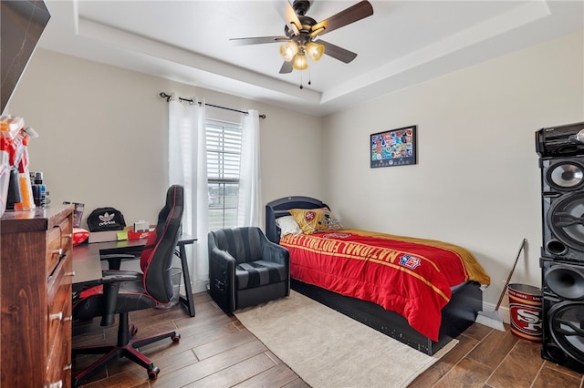 bedroom with dark wood-type flooring, ceiling fan, and a tray ceiling