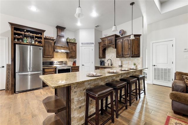 kitchen featuring dark brown cabinets, appliances with stainless steel finishes, a breakfast bar area, and custom exhaust hood