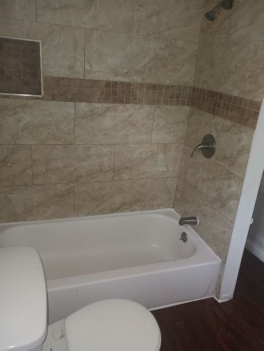 full bath with toilet, wood finished floors, and  shower combination