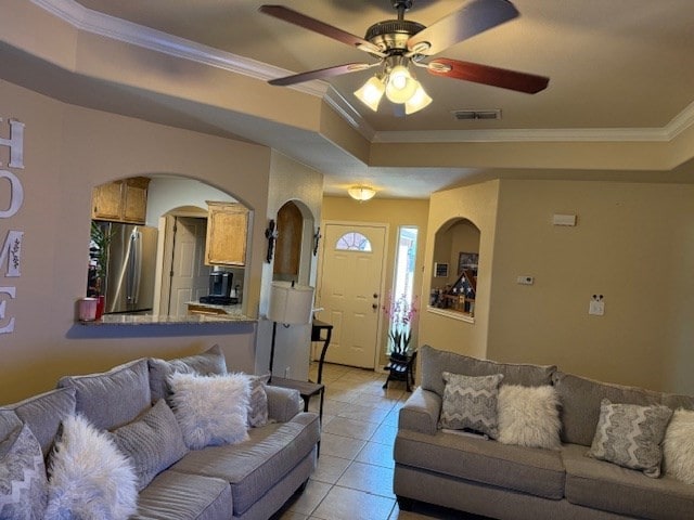 1002 Blue Crest Ln, Beeville, TX 78102 - living room featuring light tile patterned flooring, ceiling fan, ornamental molding, arched walkways, and a tray ceiling