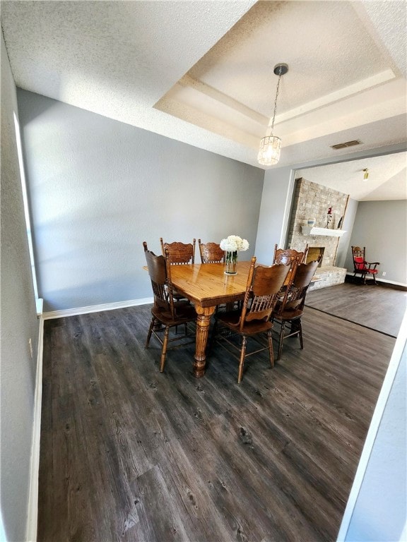 dining area featuring dark wood-type flooring, a stone fireplace, a textured ceiling, and a raised ceiling