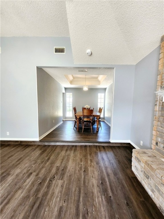 dining space with dark wood-type flooring, a stone fireplace, a textured ceiling, and a raised ceiling