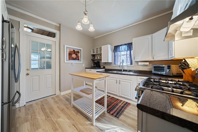 kitchen with sink, hanging light fixtures, stainless steel fridge, white cabinets, and exhaust hood