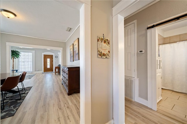 corridor with light wood-type flooring, a barn door, and ornamental molding