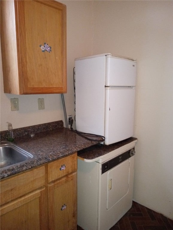 kitchen featuring dark stone counters, sink, white refrigerator, and washer / dryer