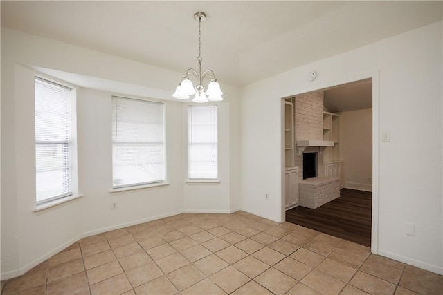 unfurnished dining area with baseboards, a chandelier, light tile patterned floors, and a fireplace