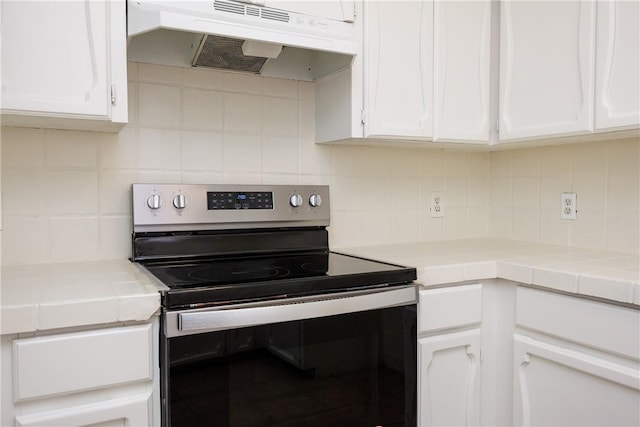 kitchen featuring tasteful backsplash, under cabinet range hood, white cabinetry, and electric stove