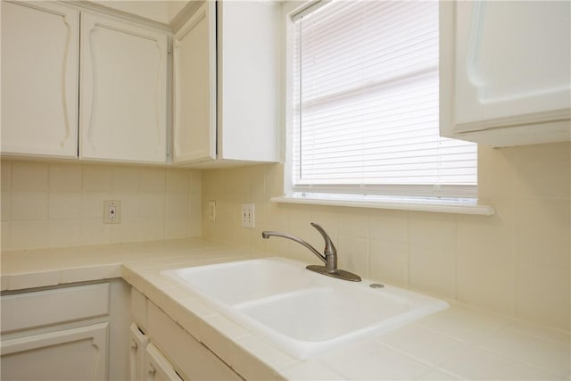 kitchen featuring a sink, decorative backsplash, tile countertops, and white cabinetry