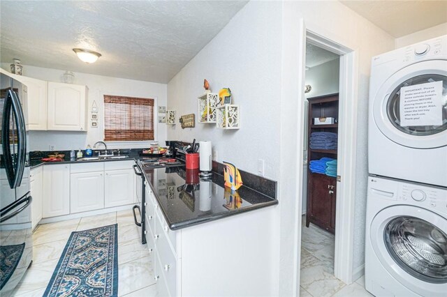 clothes washing area with stacked washer / drying machine, light marble finish flooring, a sink, and a textured ceiling
