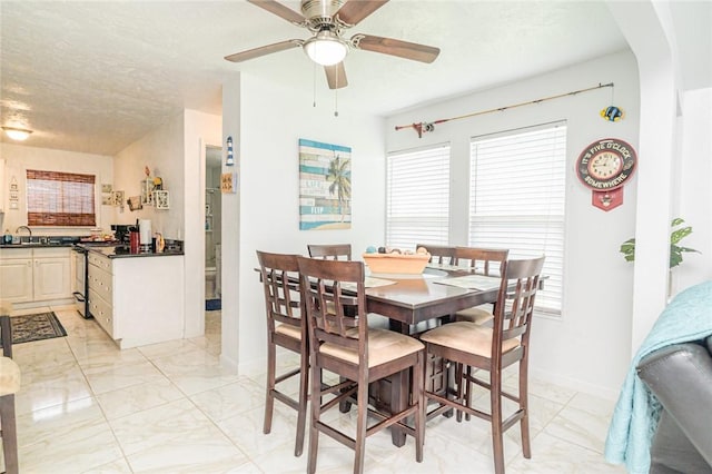 dining room featuring light marble finish floors, a ceiling fan, and baseboards