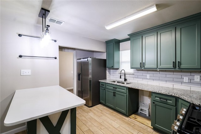 kitchen with green cabinets, stainless steel fridge with ice dispenser, sink, and hanging light fixtures