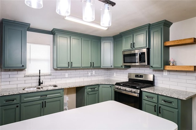 kitchen with pendant lighting, backsplash, sink, green cabinetry, and appliances with stainless steel finishes