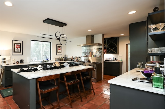 kitchen featuring a kitchen breakfast bar, wall chimney exhaust hood, decorative light fixtures, a kitchen island, and stainless steel range